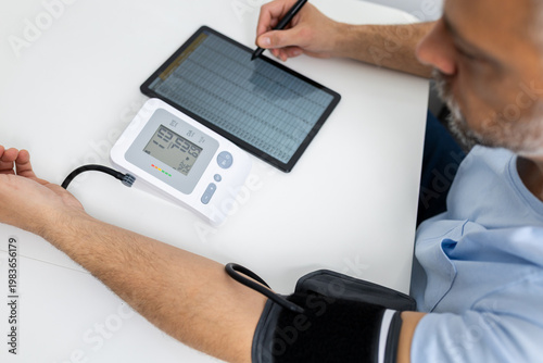 Man measuring blood pressure at home and recording results on digital tablet