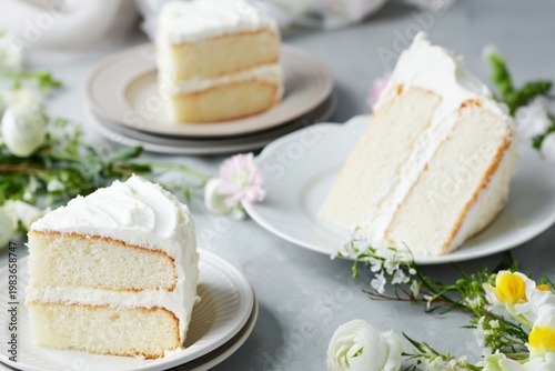 Freshly Sliced Vanilla Cake With White Frosting and Flowers on the Table