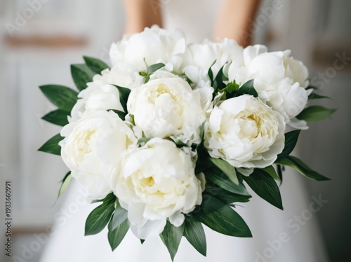 Hands Holding a Bouquet of White Peonies and Green Leaves Indoors at a Weddin...