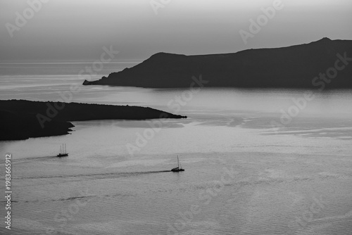 Beautiful view of two sailing boats next to the volcano Palea Kameni in Santorini Greece in black and white