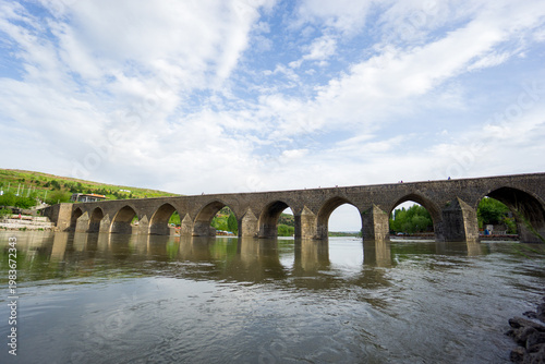 View of the historic Ten Arches Bridge (On Gozlu Bridge) spanning the Tigris River. Built during the Artuqid period, the stone bridge features multiple arches and reflects the architectural heritage o