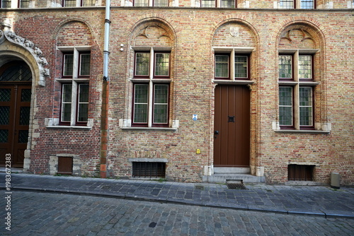 Prachtvoller alter Hauseingang mit Rundbogen in der Fassade aus Backstein eines Altbau mit Kopfsteinpflaster bei Sonnenschein in den Gassen der Altstadt von Brügge in Westflandern in Belgien