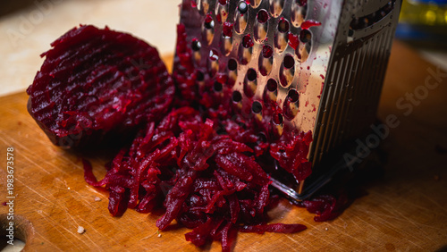 Macro of boiled red beetroot being grated on a metal grater on a wooden board. Healthy cooking process for salad or borscht. Vibrant magenta vegetable food texture