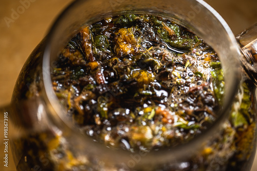 Macro shot of brewing herbal tea in a glass teapot. Natural organic infusion of tea leaves and dried flowers. Wellness, relaxation and healthy lifestyle concept