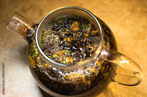 Macro shot of brewing herbal tea in a glass teapot. Natural organic infusion of tea leaves and dried flowers. Wellness, relaxation and healthy lifestyle concept