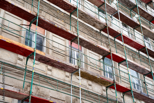 Construction scaffolding is prominently featured against a historical building facade, showcasing restoration work. The vibrant color of wooden planks contrasts with the structural elements.