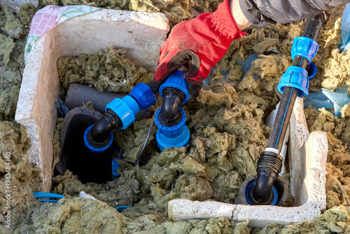 Homeowner tightening plastic compression fitting nut during installation of distribution piping in artesian well pit.