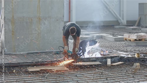 Workers using a grinder at a construction site. Work process at a construction site. Construction of an industrial building from the inside.