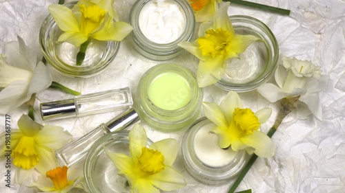Jars with face and hand cream, extract, fresh flowers daffodil are on a white background, cosmetics based on daffodils