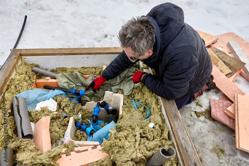 Plumber installing well pit distribution piping in winter in snowy rural area.