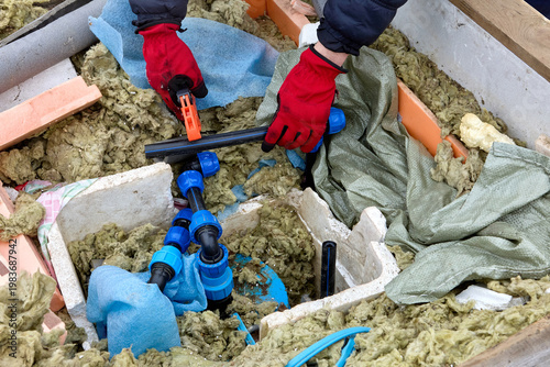 Well contractor using ratchet pipe cutter working on distribution manifold with service lines in well pit.