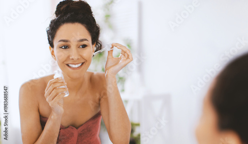 Canvas Print A woman smiles while holding a skincare product in front of a mirror