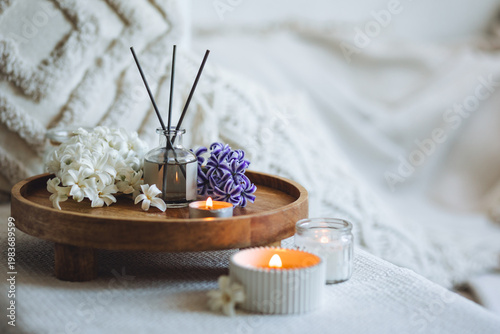 Comfortable atmosphere, spring delicious fresh smell. Aroma diffuser, burning candle, blooming hyacinth flowers and perfume on wooden bamboo tray. Cozy home decor, hygge and aromatherapy concept.