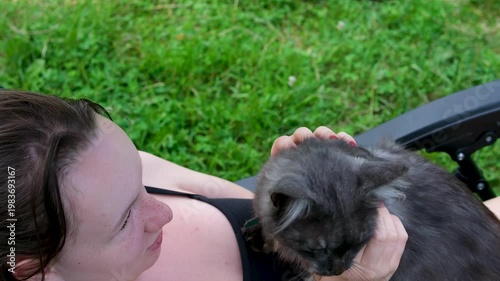 Teen girl with red manicure sitting on chair outdoors petting gray scruffy cat playful interaction rustic backyard scene