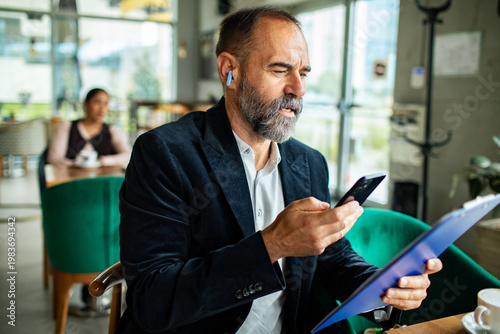 Photography Mature businessman dictating on smartphone at cafe table