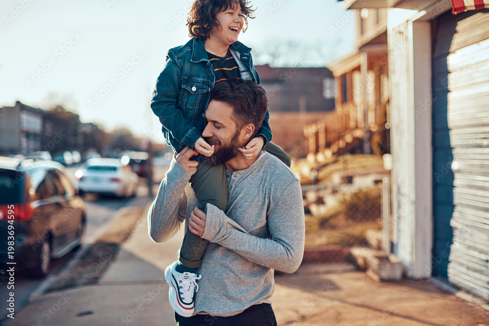 Fototapeta premium Father giving child a shoulder ride on a suburban street