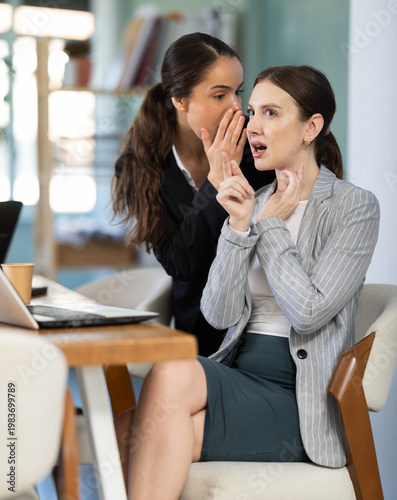 Foto Curious female employee sharing gossip with surprised young colleague during wor