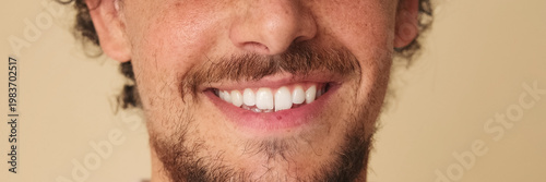 Detailed close-up shot of man's smile in studio on beige background. Panoramic