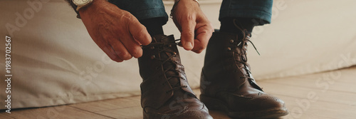Close-up of legs of mature man putting on casual boots, tying shoelaces. Panoramic