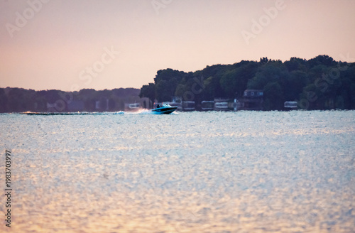 Motorboat cruising across a calm lake during a hazy summer sunrise in Waukesha County, Wisconsin. Early morning July light on the water.