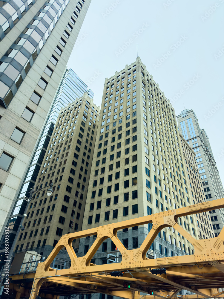 Naklejka premium Buildings and yellow bridge seen from ground level in a city on a cloudy day