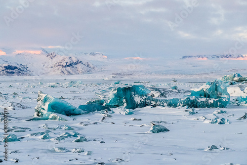 Icebergs and huge chunks for green-blueish ice fill Jokulsarlon Glacier lagoon, as the golden hour sunlight of the early morning casts a beautiful warm glow over the glacier-filled national park in