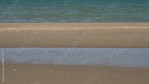 Sand bar lagoon lake with calm coastal waters shaped by littoral drift near open sea. Natural barrier beach creates shallow water and gentle ripples along shoreline beside sandbar.