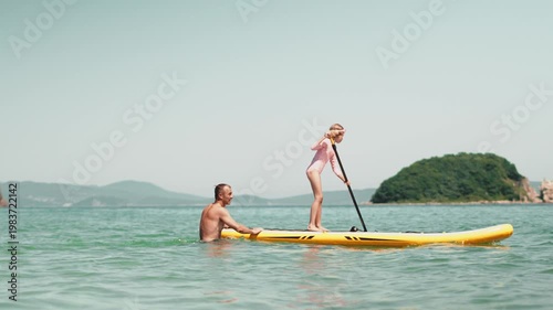 Happy child learning paddleboarding with dad in calm sea. Family vacation, outdoor activity, summer travel and healthy lifestyle on sunny beach day