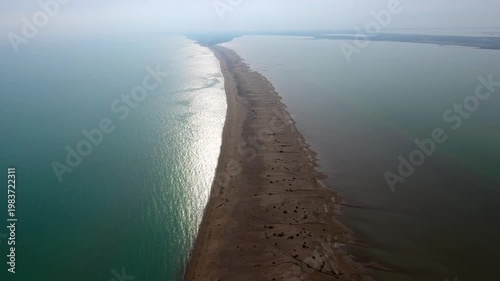 Aerial view of long thin sand tombolo separating turquoise sea and calm coastal lagoon landscape. This natural formation shows sandy barrier dividing open water shallow lake area in goksu delta.