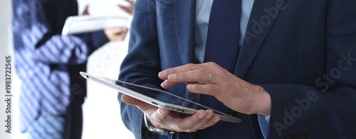 Foto Businessman in a blue suit using a tablet during a corporate meeting, interacting with the touchscreen as blurred colleagues collaborate in the background, in office