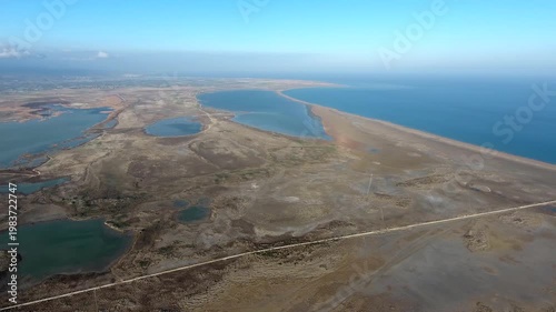 Aerial view of long thin sand tombolo separating turquoise sea and calm coastal lagoon landscape. This natural formation shows sandy barrier dividing open water shallow lake area in goksu delta.