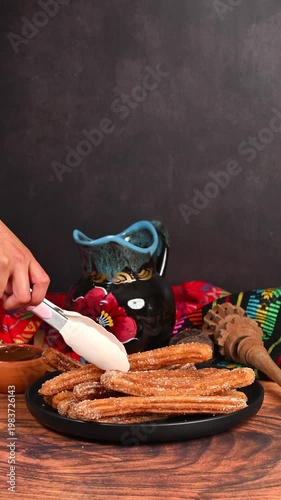 Hands placing a freshly fried churro onto a plate using silicone tongs