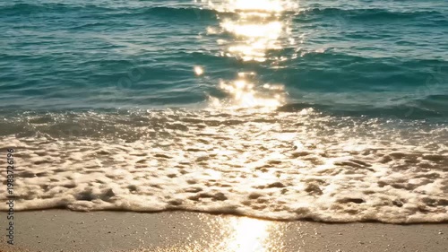 Summer day sunlight shimmering on gentle ocean waves breaking on a sandy beach at sunset. Summer vacation aesthetic video.
