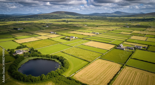 Aerial view of picturesque Irish countryside with patchwork fields small lake and distant mountains under a cloudy sky