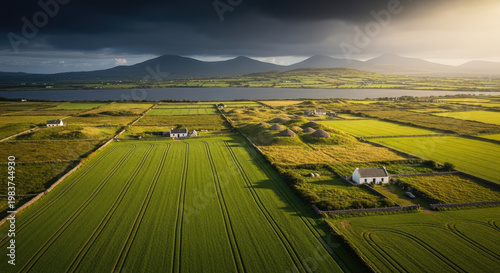 Scenic aerial view of agricultural landscape with green fields farmlands rural houses and mountains under dramatic sunlight