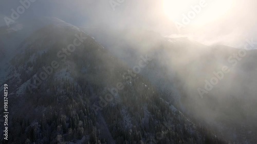 Aerial clouds drifting above snowy mountain ranges and deep alpine valleys in winter light. Layered vapor, icy summits, dramatic heights, cold wilderness, panoramic highland scenery.