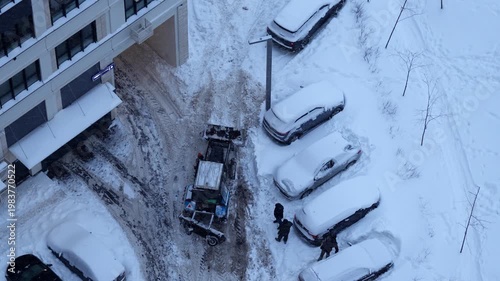 Snow removal in residential yard, tractor clearing parking area and road after snowfall, winter urban maintenance