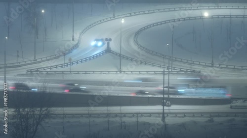 Night highway interchange in snowfall, cars moving on snowy roads, winter traffic, low visibility urban transport scene