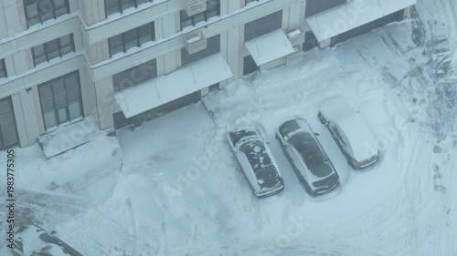 Snow covered residential parking lot during winter storm, cars buried in snow, cold urban weather, snowfall aftermath