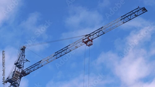 Construction crane lifting materials against a blue sky with clouds, showcasing the mechanical arm's movement and operational capabilities in an urban environment