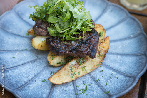  grilled steak served on a bed of thick-cut fries and topped with a fresh arugula salad. 
The steak appears to be a hanger or sirloin cut, cooked to a char on the outside.
