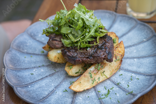  grilled steak served on a bed of thick-cut fries and topped with a fresh arugula salad. 
The steak appears to be a hanger or sirloin cut, cooked to a char on the outside.
