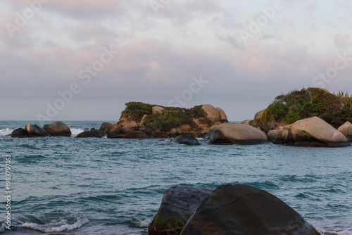 Coastal paradise view with boulders along surf line, calm sea movement
