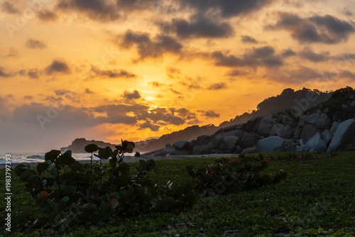 Seaside landscape at dusk with sun near horizon, crashing waves, and silhouetted coastal rocks