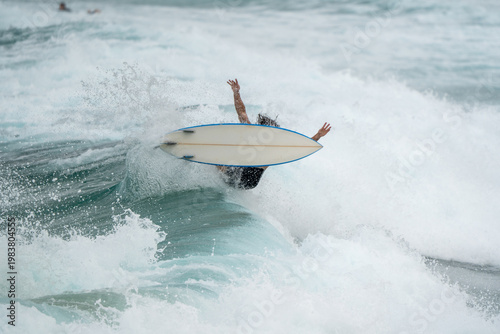 Surfer falling off board in powerful surf with huge splash, action ocean sports scene