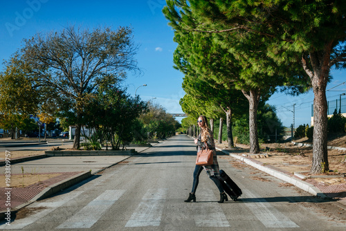 Businesswoman pulling rolling luggage across crosswalk on sunny day
