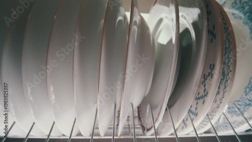 Clean White Ceramic Plates Stacked on Metal Dish Rack Inside Kitchen Cabinet | Organized Dishware Storage | Close-Up Wide-Angle View
