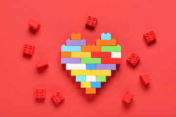 Heart made of colorful plastic building blocks on red background