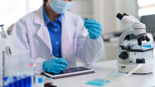Asian adult scientist researcher analyzes medical sample data holds test tube inputs experiment results digital tablet modern laboratory setting