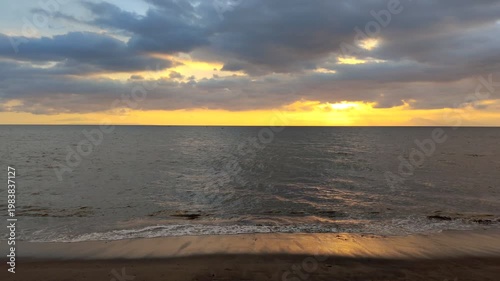 A seascape with calm waves and a sunset obscured by clouds